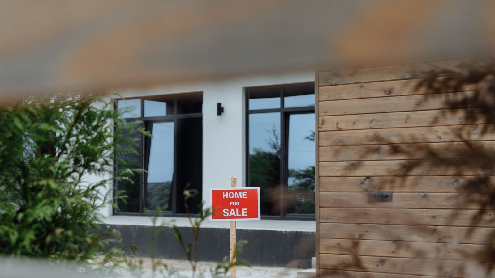 A contemporary home with a For Sale sign in the front yard, representing rising mortgage rates and housing affordability