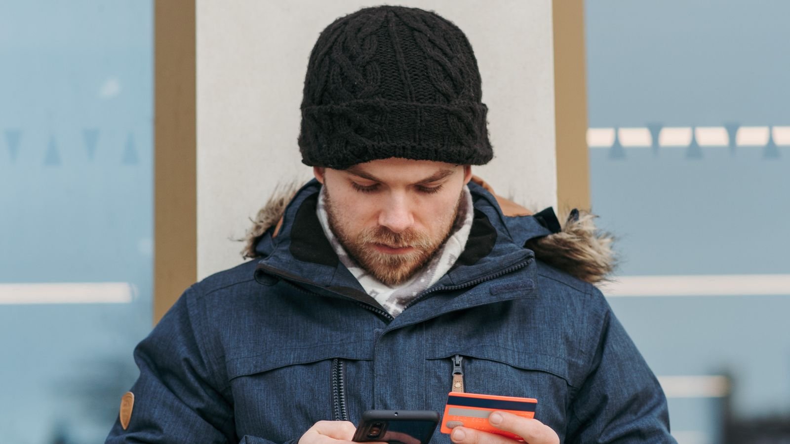A young man using a smartphone and credit card while shopping outdoors, representing US retail sales and consumer spending