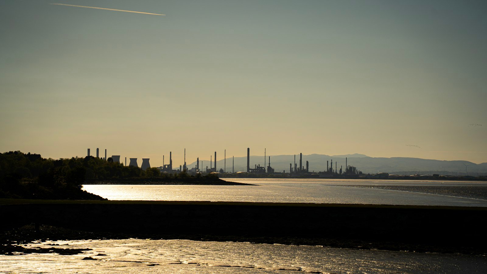Oil refineries and cooling towers silhouetted at sunset beside an estuary